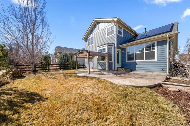 rear view of property with a yard, a patio, solar panels, board and batten siding, and a pergola