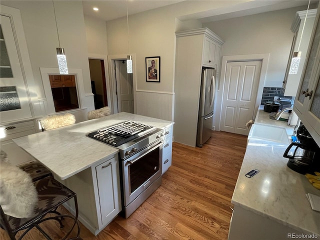 2335 Stout St, Denver, CO 80205 - kitchen featuring appliances with stainless steel finishes, light wood-style floors, white cabinets, light stone counters, and wainscoting