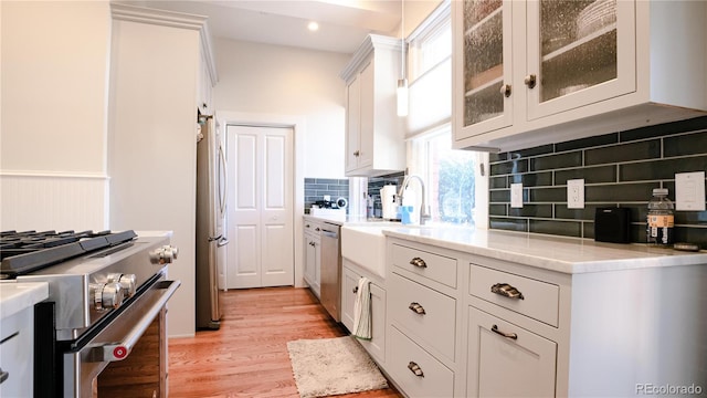 2335 Stout St, Denver, CO 80205 - kitchen with appliances with stainless steel finishes, a sink, tasteful backsplash, light wood-type flooring, and glass insert cabinets