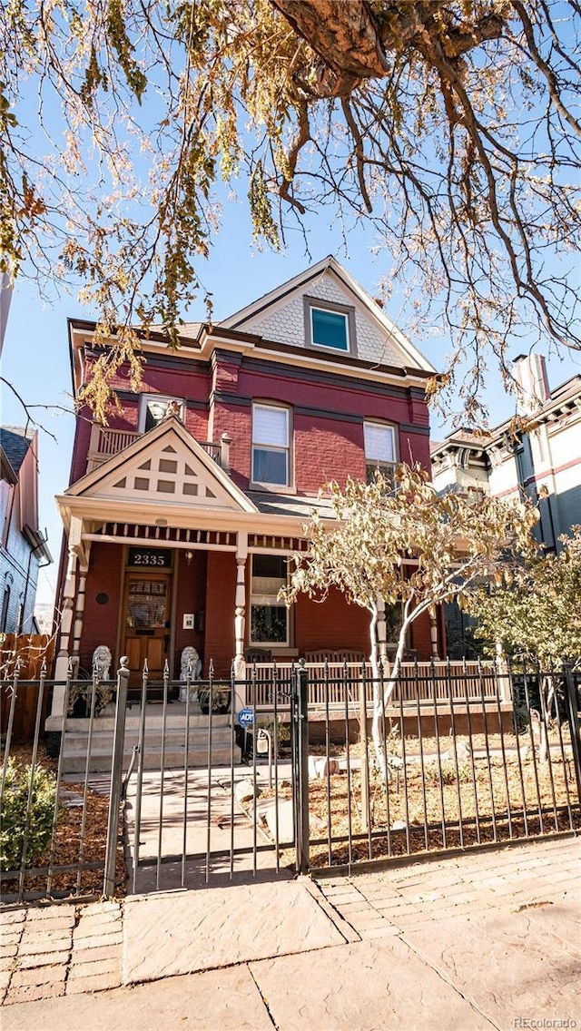 2335 Stout St, Denver, CO 80205 - victorian-style house featuring a porch, a fenced front yard, a gate, and brick siding