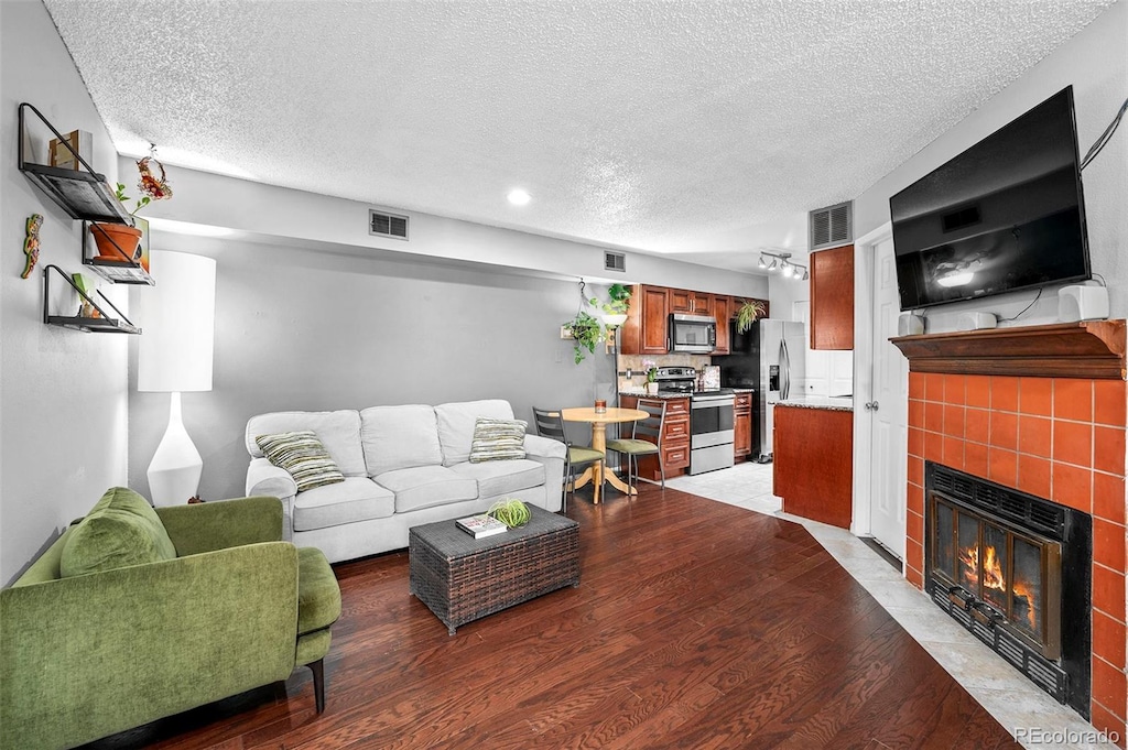 living room with a textured ceiling, wood-type flooring, and a tile fireplace