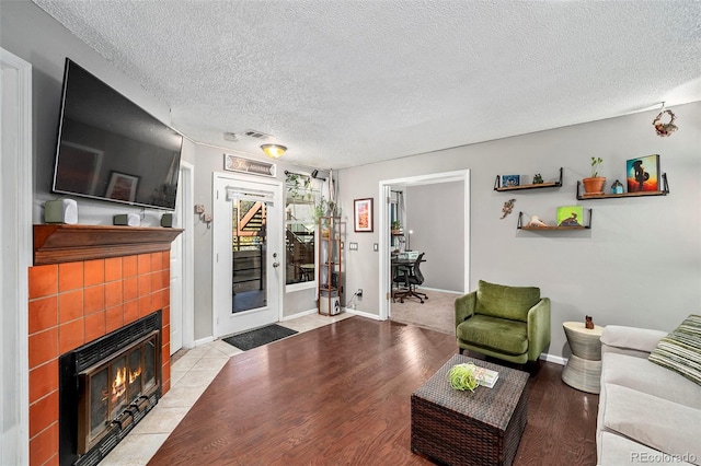 living room with a tiled fireplace, light hardwood / wood-style floors, and a textured ceiling