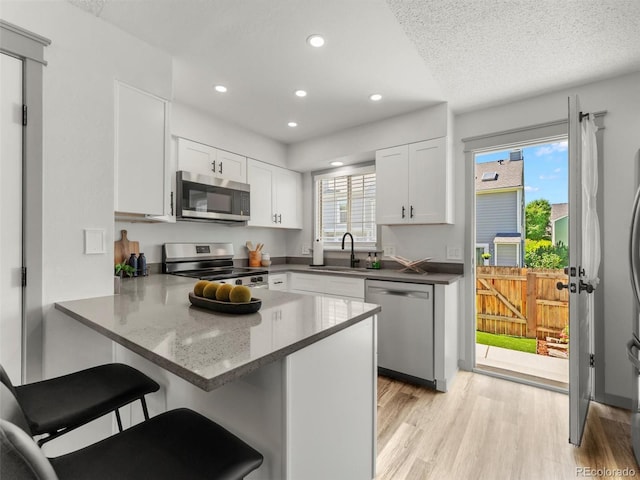 19726 Applewood Ct, Parker, CO 80138 - kitchen featuring appliances with stainless steel finishes, a peninsula, white cabinets, light wood-type flooring, and a kitchen breakfast bar