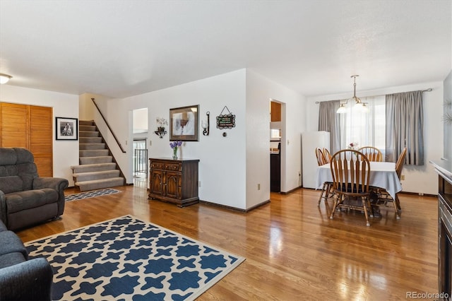 living room featuring baseboards, stairway, an inviting chandelier, and wood finished floors