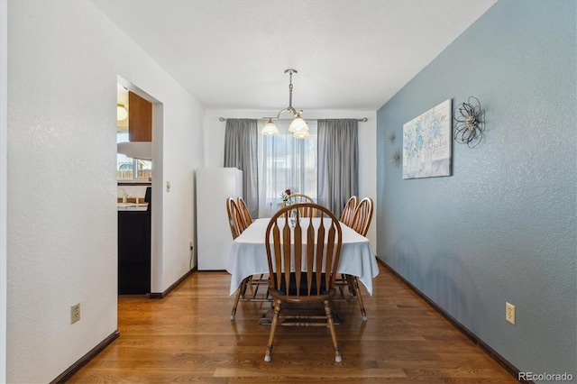 dining area with an inviting chandelier, baseboards, wood finished floors, and a textured wall