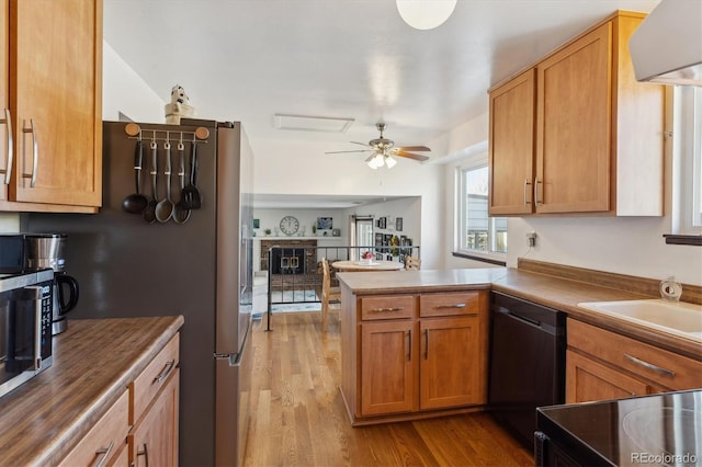 kitchen with a peninsula, wood finished floors, open floor plan, a brick fireplace, and dishwasher