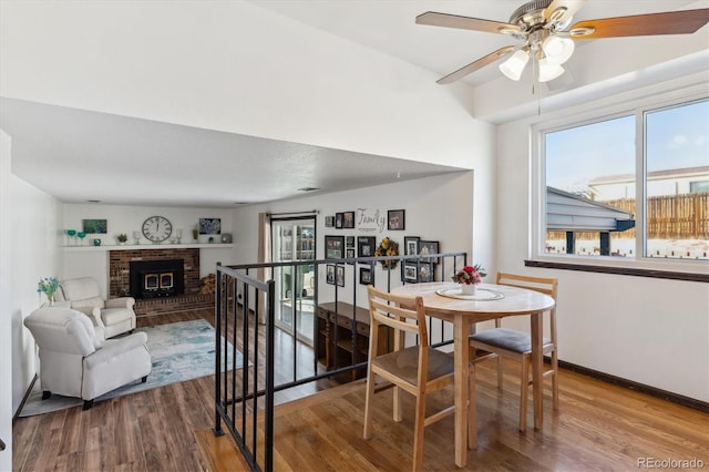 dining area featuring baseboards, a brick fireplace, wood finished floors, and a healthy amount of sunlight