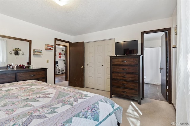 bedroom with ensuite bath, a textured ceiling, a closet, and light colored carpet