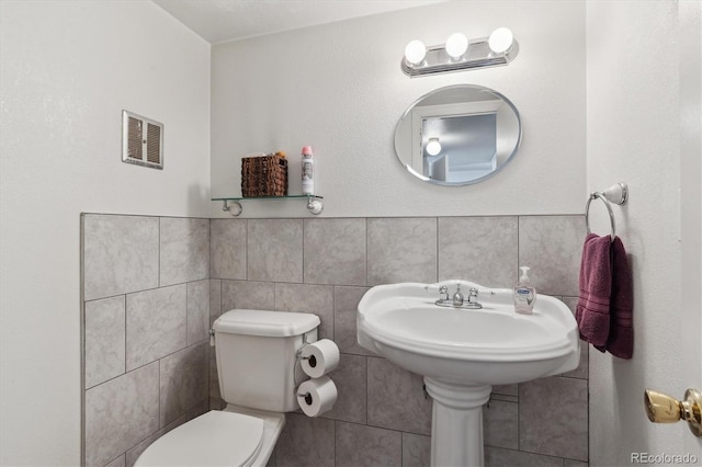 half bathroom featuring toilet, a wainscoted wall, visible vents, and tile walls