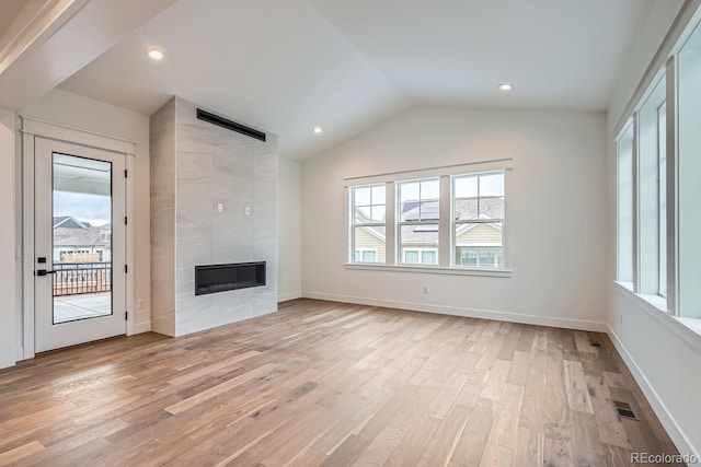 unfurnished living room with lofted ceiling, a tile fireplace, and light hardwood / wood-style flooring