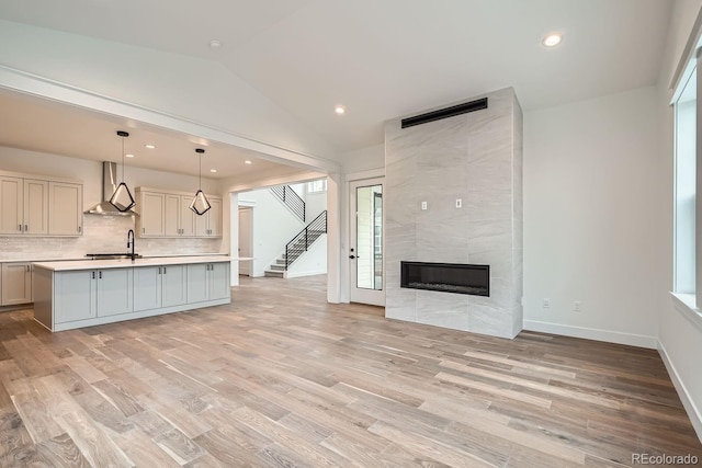 kitchen with decorative light fixtures, a tile fireplace, wall chimney exhaust hood, lofted ceiling, and a center island with sink