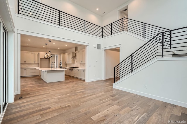 unfurnished living room featuring a towering ceiling, sink, and light hardwood / wood-style flooring