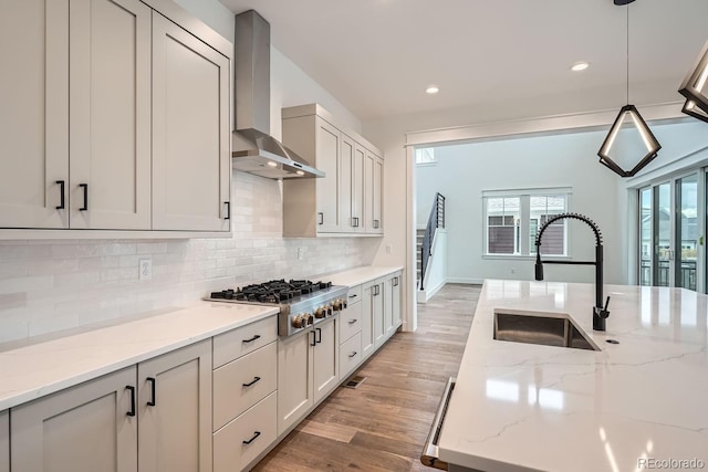 kitchen featuring light stone countertops, wall chimney exhaust hood, decorative light fixtures, stainless steel gas cooktop, and sink