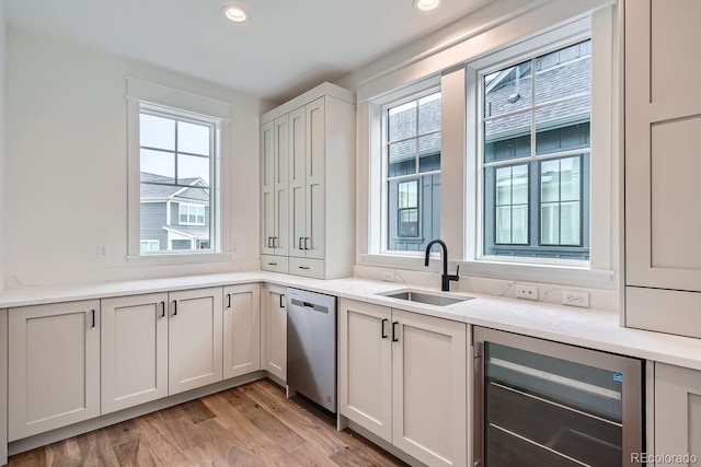 kitchen with beverage cooler, white cabinets, sink, light hardwood / wood-style flooring, and stainless steel dishwasher