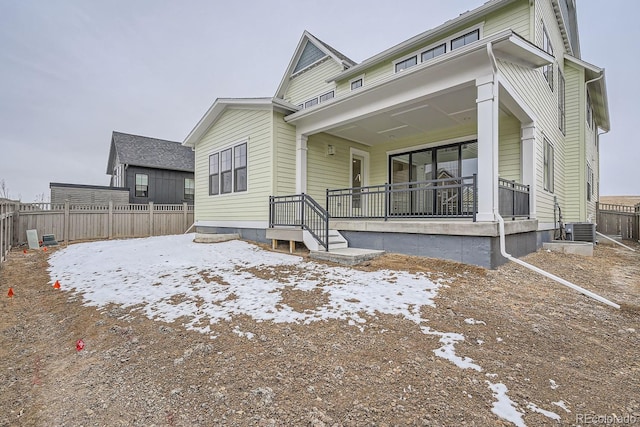 snow covered back of property featuring covered porch and cooling unit