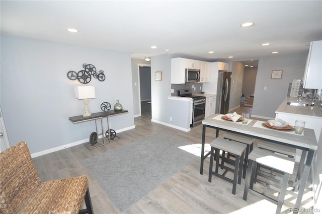 kitchen with appliances with stainless steel finishes, white cabinetry, sink, backsplash, and light wood-type flooring