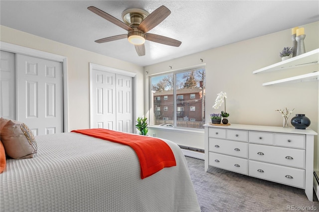 bedroom with two closets, a textured ceiling, carpet flooring, a baseboard radiator, and ceiling fan