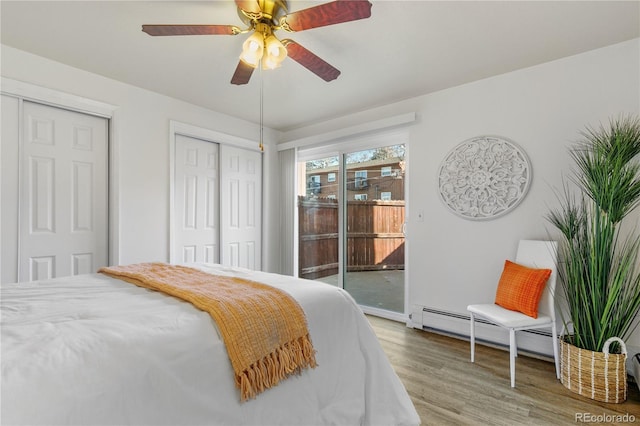 bedroom featuring a ceiling fan, wood finished floors, two closets, access to exterior, and baseboard heating