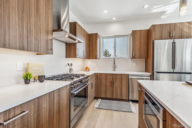 kitchen featuring sink, premium appliances, wall chimney range hood, light stone countertops, and light hardwood / wood-style floors