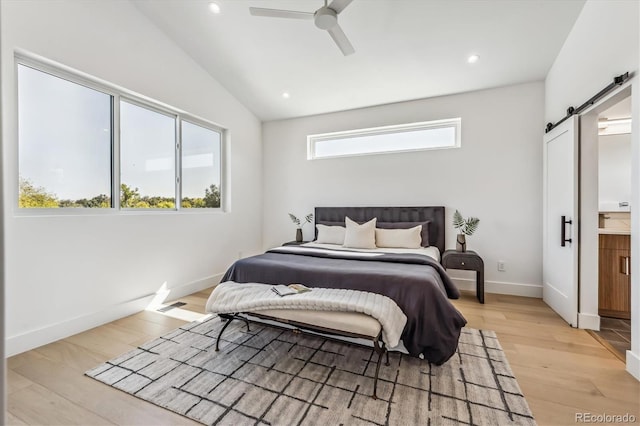 bedroom featuring light wood-type flooring, ceiling fan, connected bathroom, a barn door, and vaulted ceiling