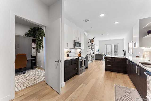 kitchen featuring appliances with stainless steel finishes, white cabinets, decorative backsplash, dark brown cabinetry, and light wood-type flooring