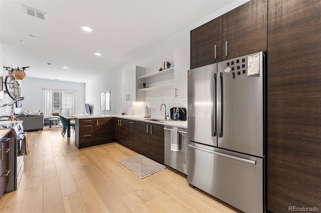 kitchen featuring sink, decorative backsplash, stainless steel appliances, dark brown cabinets, and light wood-type flooring