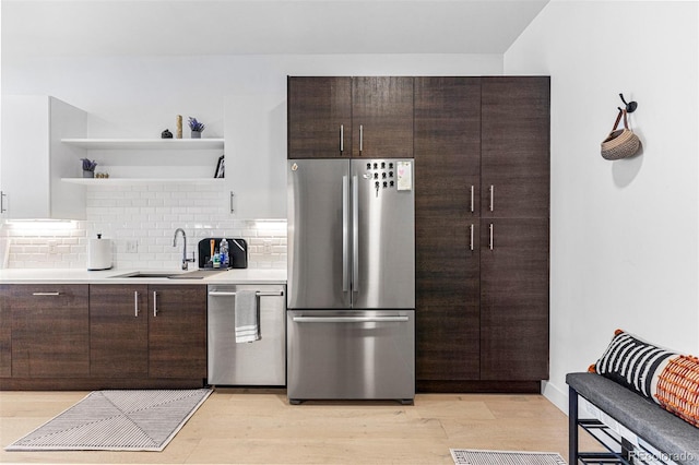 kitchen with sink, backsplash, stainless steel appliances, dark brown cabinets, and light hardwood / wood-style flooring