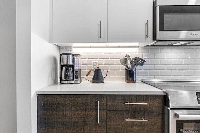 kitchen with dark brown cabinetry, backsplash, white cabinets, and appliances with stainless steel finishes