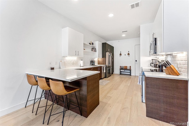 kitchen featuring appliances with stainless steel finishes, a breakfast bar, white cabinetry, kitchen peninsula, and light wood-type flooring