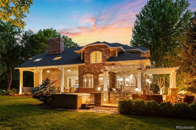 back of property featuring a shingled roof, stone siding, a lawn, and a chimney