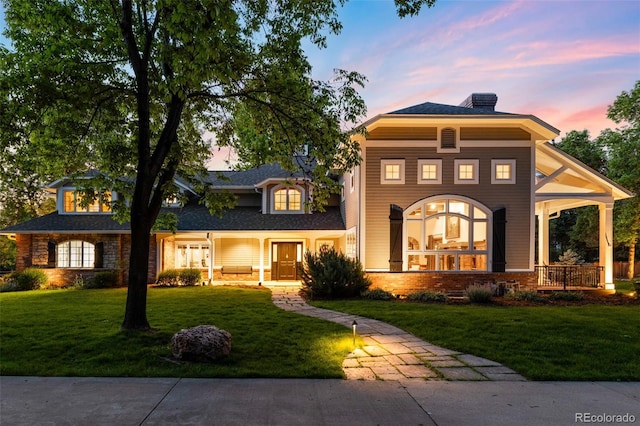 view of front facade featuring covered porch, a front lawn, a chimney, and brick siding