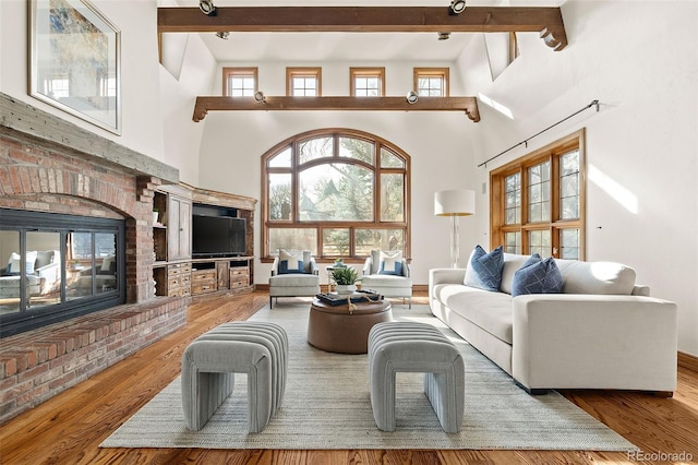 living room featuring a wealth of natural light, a brick fireplace, wood finished floors, and beam ceiling