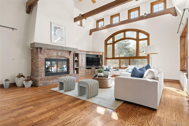 living area with a high ceiling, plenty of natural light, wood finished floors, and a brick fireplace