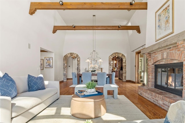 living area with arched walkways, a brick fireplace, beamed ceiling, and wood finished floors