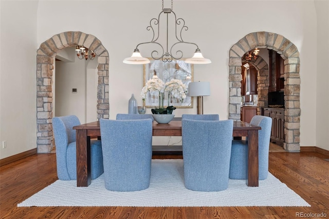 dining area with arched walkways, baseboards, and wood finished floors