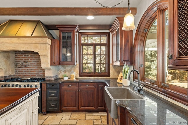 kitchen with beam ceiling, stone tile flooring, backsplash, gas stove, and a sink