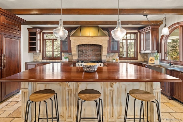 bar featuring tasteful backsplash, stone tile flooring, stainless steel gas stovetop, paneled built in refrigerator, and premium range hood