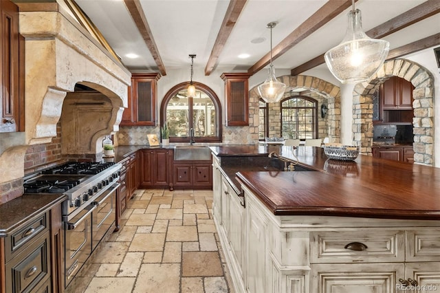 kitchen featuring stone tile floors, a sink, butcher block countertops, double oven range, and plenty of natural light