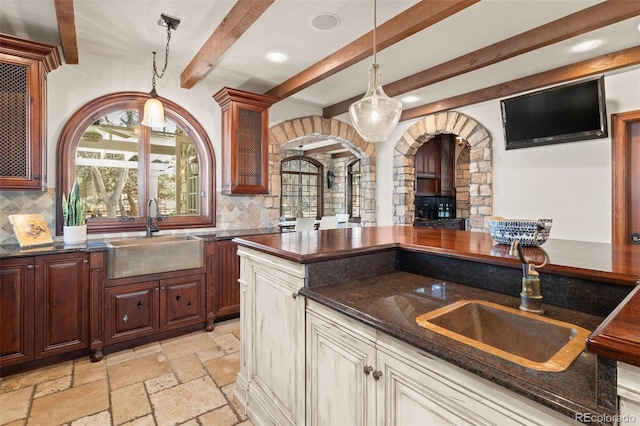 kitchen with hanging light fixtures, stone tile floors, decorative backsplash, and a sink