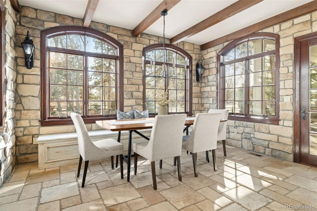 dining space featuring stone tile flooring and beamed ceiling