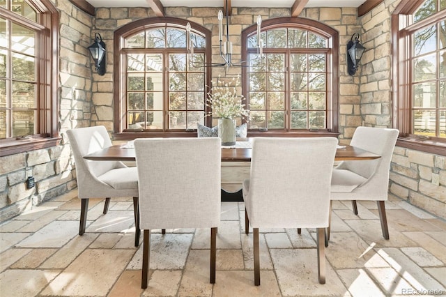 dining space with beam ceiling and stone tile flooring