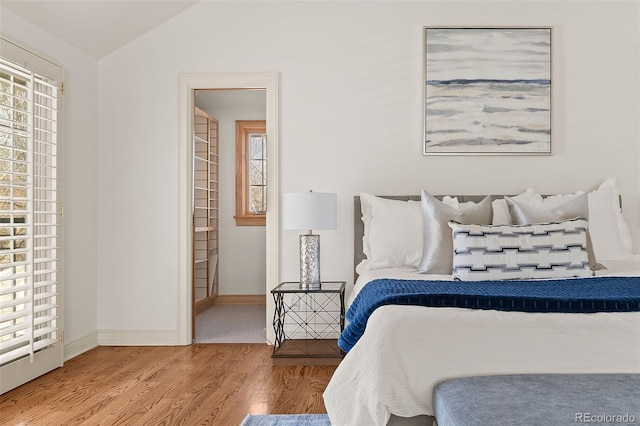 bedroom featuring lofted ceiling, baseboards, and wood finished floors