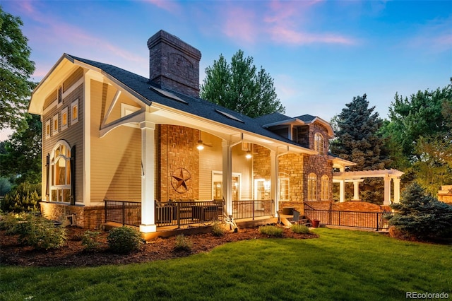 back of property featuring a yard, a porch, a chimney, and stone siding