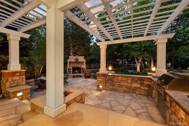 view of patio / terrace with exterior kitchen, an outdoor stone fireplace, a grill, and a pergola