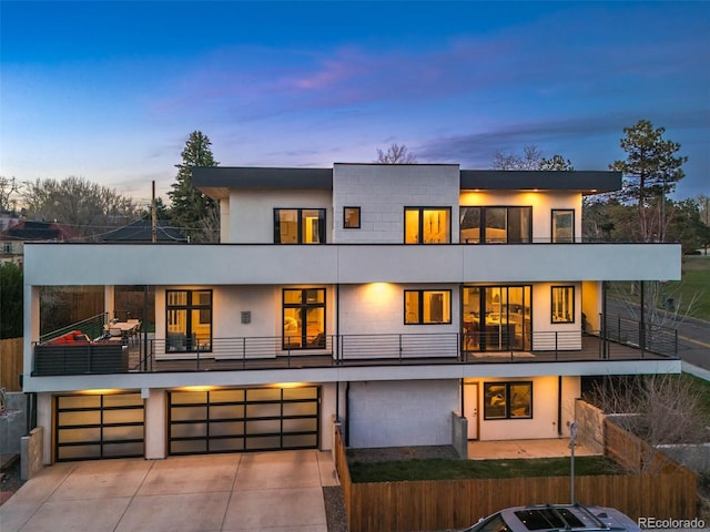 back of property with an attached garage, driveway, a balcony, and fence