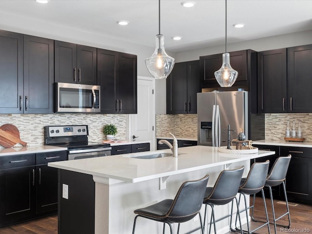 kitchen featuring appliances with stainless steel finishes, sink, dark hardwood / wood-style flooring, hanging light fixtures, and a center island with sink