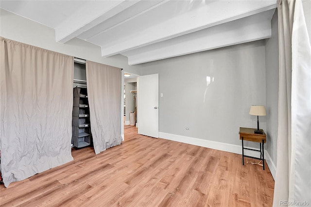 unfurnished bedroom featuring beamed ceiling, baseboards, and wood finished floors