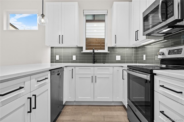 kitchen with sink, light hardwood / wood-style flooring, pendant lighting, stainless steel appliances, and white cabinets