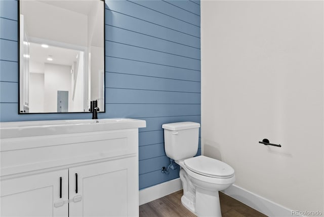 bathroom with wooden walls, vanity, toilet, and wood-type flooring