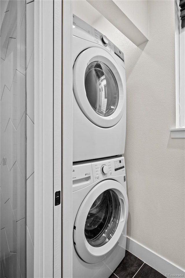 laundry room featuring stacked washer and dryer and dark tile patterned floors